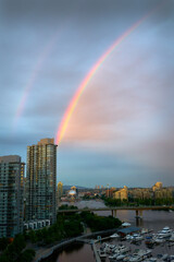 Obraz premium False Creek Rainbow. A rainbow across False Creek at dusk over the Cambie Bridge and towers in Vancouver. British Columbia, Canada.