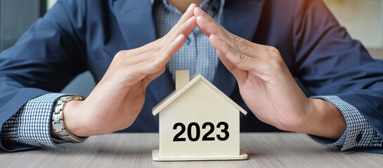 Businessman hands over wooden House model with 2023 New Year text. Property insurance and real estate concepts
