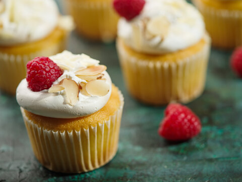Many appetizing muffins with cream, raspberries and almonds on a green background. Large group of objects. Food design, restaurant, hotel, cafe, patisserie, home cooking.