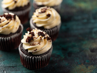 Lots of chocolate cupcakes with cream and chocolate chips on a dark background. Birthday, treat, sweet food. Restaurant and home cooking, cookbook, culinary blog. Advertising, invitation.