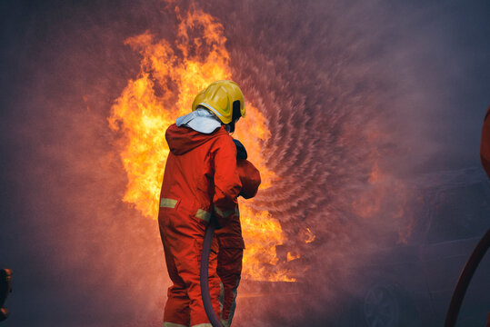 Firefighter Rescue training in fire fighting extinguisher. Firefighter fighting with flame using fire hose chemical water foam spray engine. Fireman wear hard hat, safety suit uniform for protection