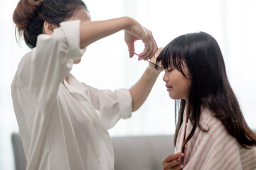 Asian Mother cutting hair to her daughter in living room at home while stay at home safe from Covid-19 Coronavirus during lockdown. Self-quarantine and social distancing concept.