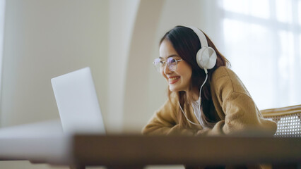 Young asian woman wearing glasses and headset working on computer laptop at house. Work at home, Video conference, Video call, Student learning online class - Powered by Adobe
