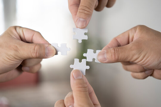 Closeup image of many people holding and putting a piece of white jigsaw