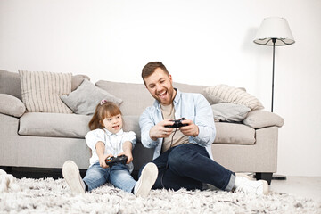 Girl with Down syndrome and her father sitting on a floor and playing PlayStation