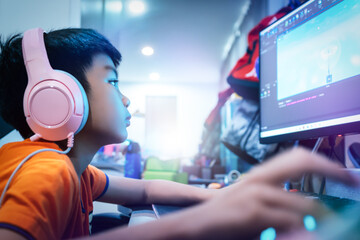Asian kid is coding and scripting program on on his game streaming desktop computer with headphone...