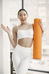 Fototapeta na wymiar Young fitness woman ready for workout holding orange yoga mat