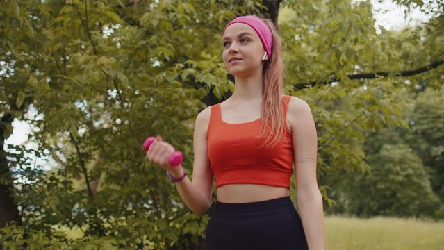 Athletic young sporty fit girl doing dumbbells workout in park performing bicep curls to build arm muscle and strength. Pretty woman enjoying exercising outdoors. Active sportswoman sport motivation