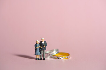 Miniature people toys conceptual photography. Elderly couple standing beside golden diamond ring....