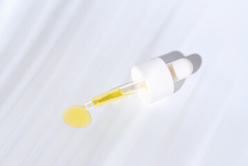 Pipette with collagen and tropical leaf shadow on white background close-up, skin care concept.