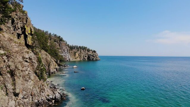 Picturesque seascape from the air. Rocks and the shore of the sea or lake on a sunny summer day. Beautiful turquoise color of the water. Pine trees on steep cliffs.
