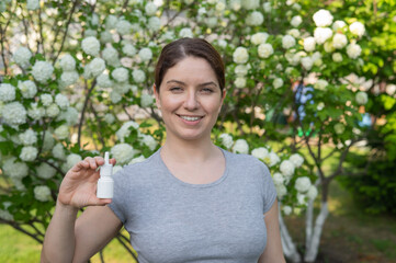 Happy woman demonstrating nasal spray on the background of a blossoming tree. 