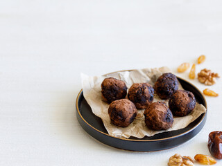 Healthy homemade delicious energy balls: chocolate ball cakes made from raisin, prune, dates, walnut, figs in black plate against white background, covered with cocoa carob powder. Close up copy space