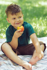 little brunettebeautiful boy eating a peach in summer park