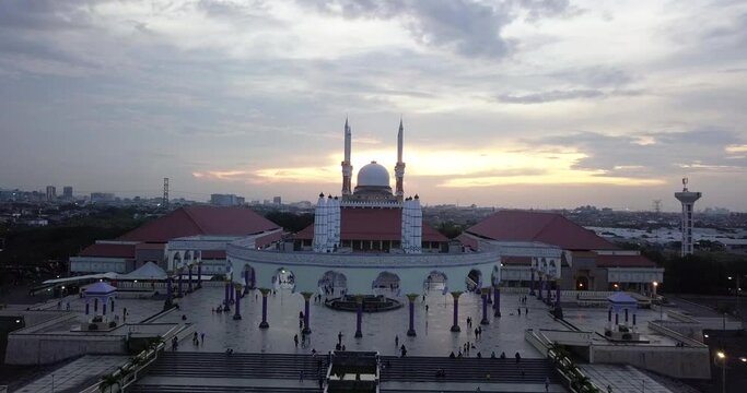 Reveal drone shot of the great Mosque of Central Java (MAJT) in suset time. Th sun is orange and the weather is cloudy. It have some pillars and some umbrela that is closed