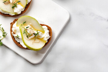 Toast with cottage cheese ricotta cheese, pear, honey and almond. Sandwiches, Bruschetta, snack, appetizers on white board. Top view, copy space.