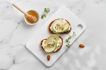 Appetizer with ricotta cheese, cream cheese, honey, pear, thyme on white board and marble table. Toast, snack, bruschetta. Top view, copy space, text