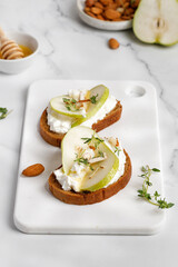 Bread toast with ricotta cheese, cream cheese, honey, almond, pear, thyme on white board and marble table. Snack, bruschetta. Close up.