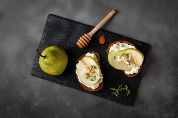 Toast with cottage cheese ricotta cheese, pear, honey and almond. Sandwiches, appetizers, bruschetta, snack on slate board and dark background. Copy space, text, top view.