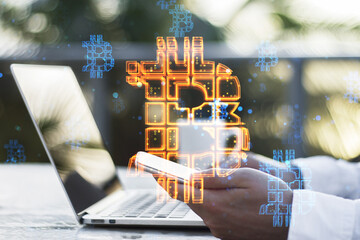 hands using laptop and cellphone with abstract glowing bitcoin sign hologram on desktop and blurry outside background. Cryptocurrency, finance, trade and market concept. Double exposure.
