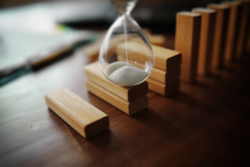 domino effect concept with wooden tiles blocked by hourglass with background