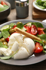 Delicious burrata salad served on wooden table, closeup