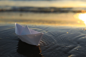 White paper boat in shallow water of sea at sunset, space for text