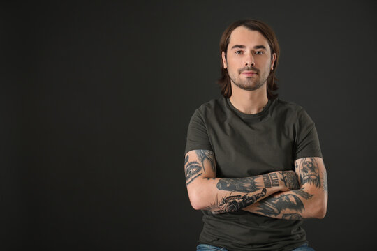 Young man with tattoos on arms against black background. Space for text