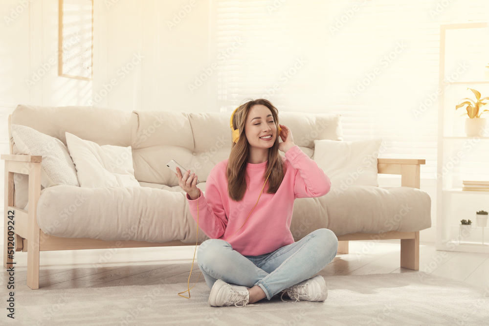 Wall mural Young woman with headphones listening to music while sitting on floor in living room