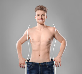 Happy young man with slim body in oversized jeans on grey background. Weight loss
