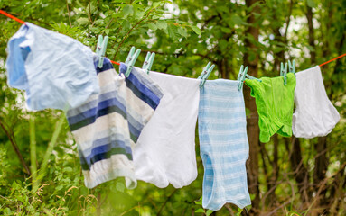 baby toddler kid clothes hanging from rope outside,nature environment.little boy in background.clean clothes outdoors,sunny summer day.housekeeping concept,baby love and care