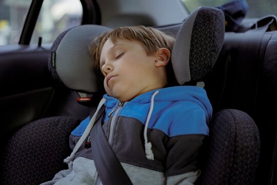 Cute Caucasian Boy Sleeping In Child Seat Fastened With Belt. Family Vacation By Car Concept