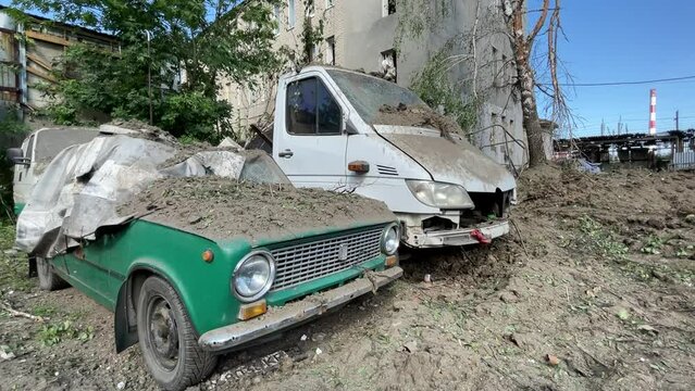 Broken cars covered with earth after shelling. Destroyed buildings in the background. The real war between Ukraine and Russia