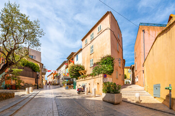 Colorful shops and buildings line the narrow, hilly alleys and streets in the Old town area of Saint-Tropez, France. - obrazy, fototapety, plakaty