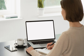 Young woman using laptop computer with white mockup screen at home. Business woman working in office. Freelance, student lifestyle, e-learning, technology and online meeting concept