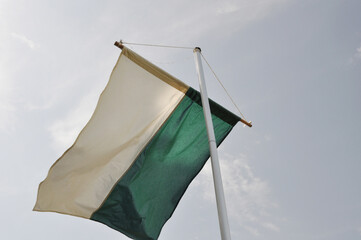 Die Schützenfestflagge ist gehisst. Die Schützenfestfahne weht im Wind vor blauen Himmel. Flaggenmast mit grünweißen Banner.