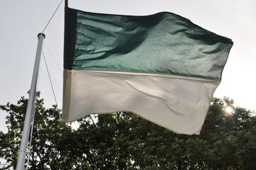 Die Schützenfestflagge ist gehisst. Die Schützenfestfahne weht im Wind vor blauen Himmel. Flaggenmast mit grünweißen Banner.