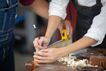 A carpenter works with equipment on a wooden table in a carpentry shop.