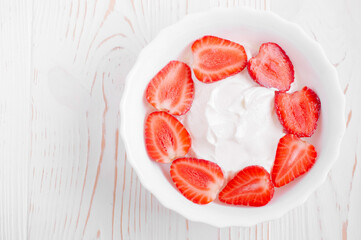 yogurt with strawberry slices in a white plate on a white wooden background