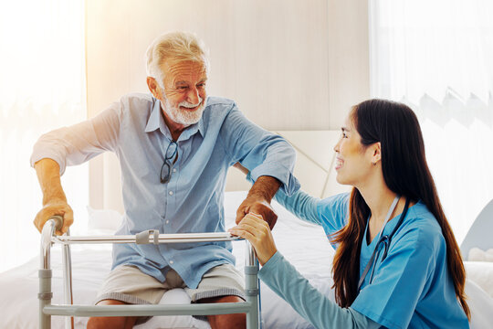 female caregiver helping elderly grandfather to walk with a walker helper and smiling in a good mood.
