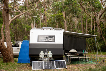 RV caravan camper on a campsite in the bush forest nature. Awning, portable toilet, solar panels, bbq, table. Family camping