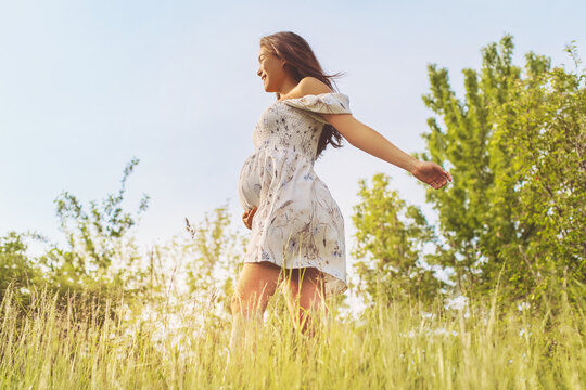 Natural pregnancy healthy Asian pregnant woman walking in nature fields for eco-friendly sustainability baby bump concept. Girl in feminine dress with open arms carefree