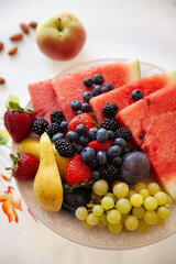 Top view on a plate with sliced fruits and berries on a beautiful white plate with fruit smoothie on the table. Watermelon, strawberry, blueberries, blackberry and grapes. Healthy snack.