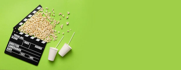 Tasty popcorn with cups of cola drink and movie clapper on green background with space for text