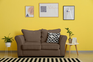 Interior of stylish living room with brown sofa and table near yellow wall