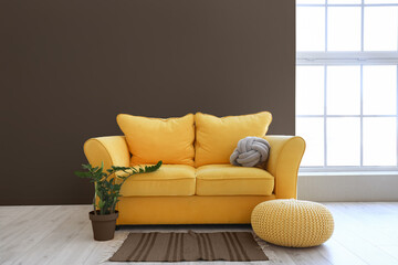 Interior of stylish living room with yellow sofa and pouf near brown wall