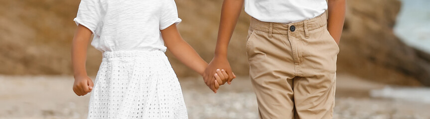Little African-American brother and sister holding hands on sea beach