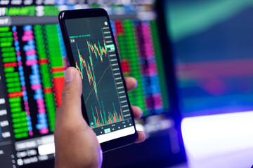 Close-up financial using smartphone analyze exchange rate diagram. Investor businessman analyzing a graphic of stock cryptocurrency exchange chart with cell phone. Investment concept