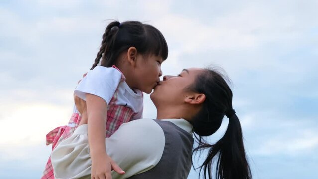 Loving mother holding a cute smiling little girl and kissing by the lake. Happy family, mother and little daughter playing feeling happy in the park.