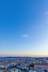 A rising moon at dusk with a view over Lisbon, Portugal and its orange colored roof tiles